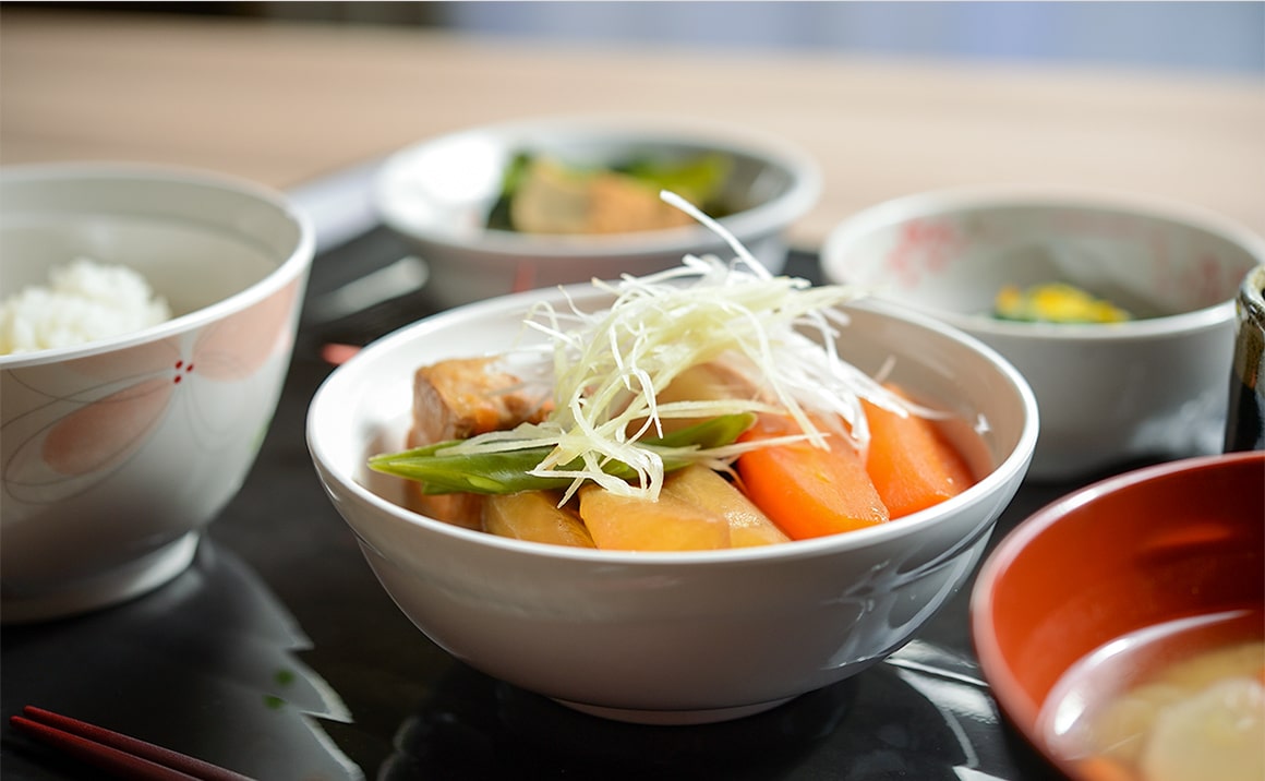 介護施設の食事。白磁の器に盛られた野菜と豚肉の煮込み料理