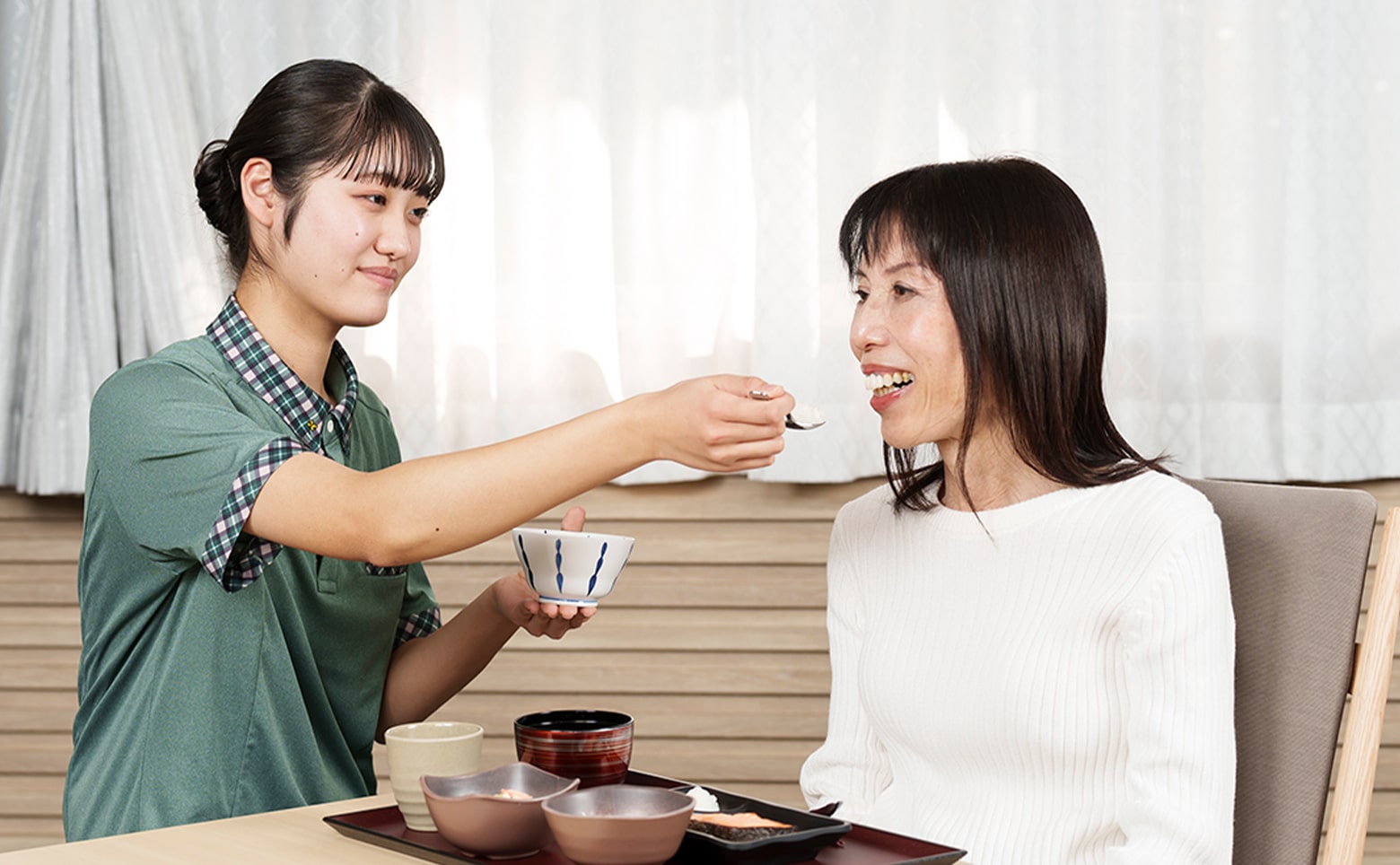 介護職員が入居者に食事を提供する様子。笑顔で温かいケアの場面。